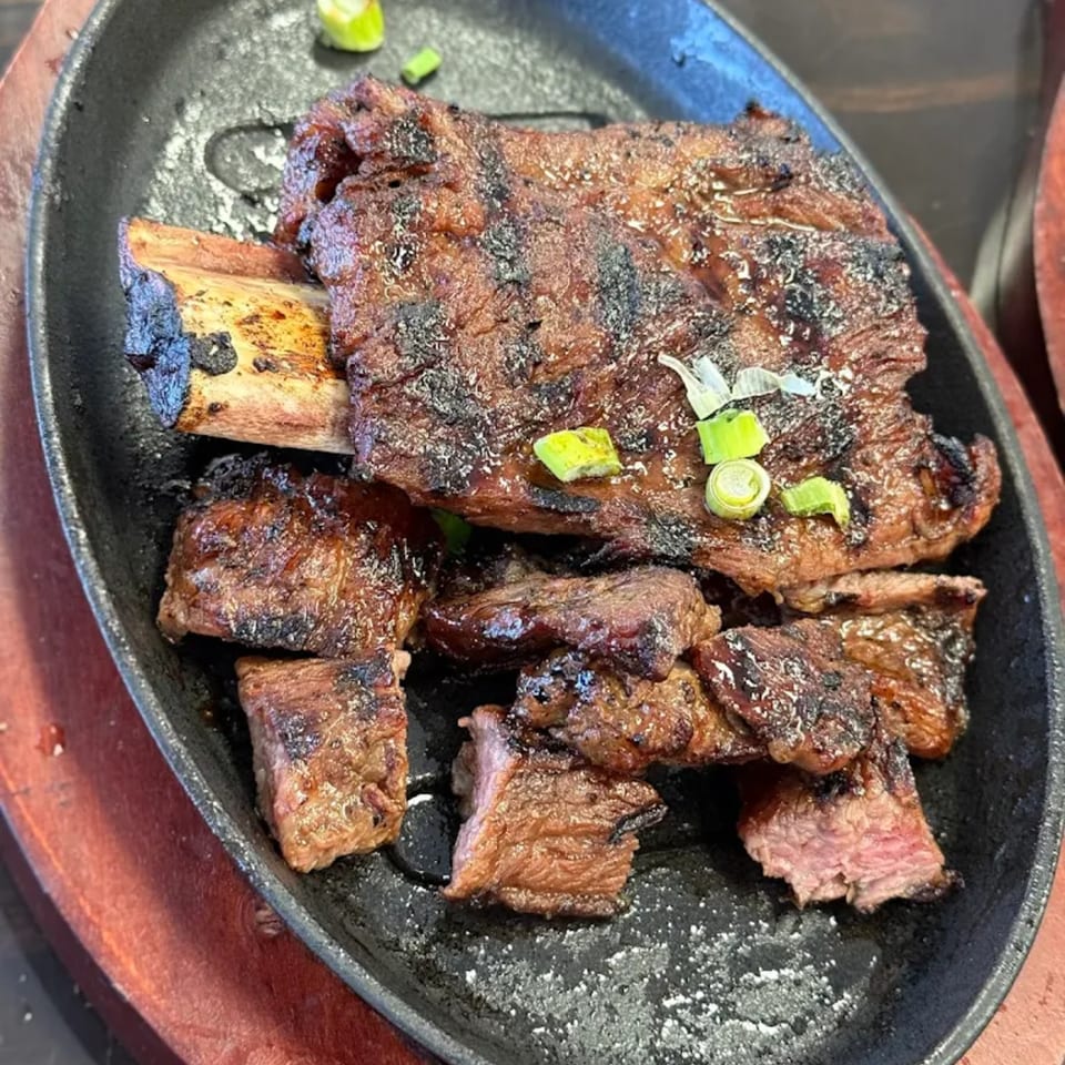 Grilled Korean BBQ short ribs (galbi) with green onions on a sizzling black plate.