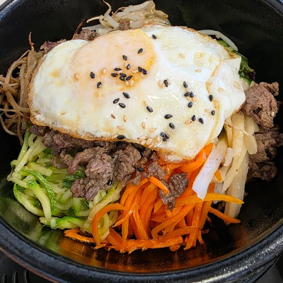 A close-up of a Korean bibimbap bowl with beef, vegetables, and a fried egg.