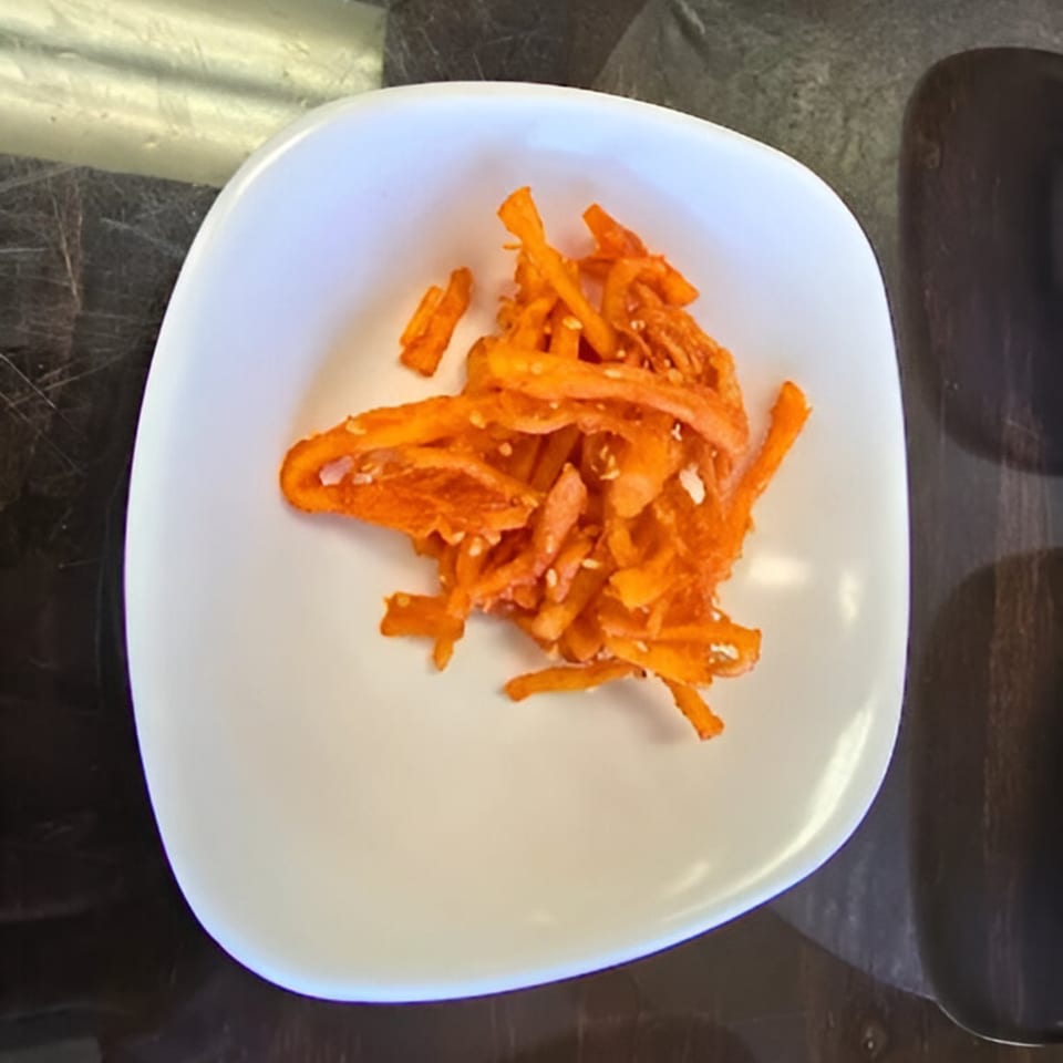 A white square bowl filled with bright orange, shredded Korean seasoned dried squid.