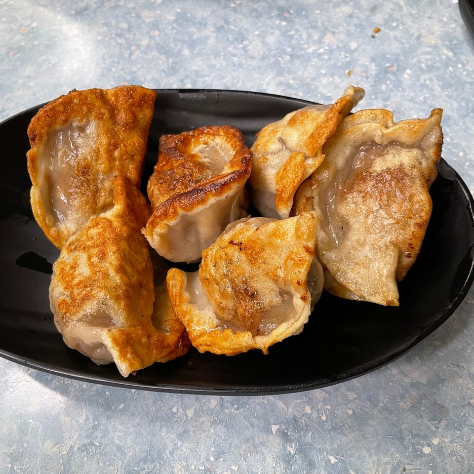 A black plate filled with several golden-brown, pan-fried Korean dumplings, glistening with oil.