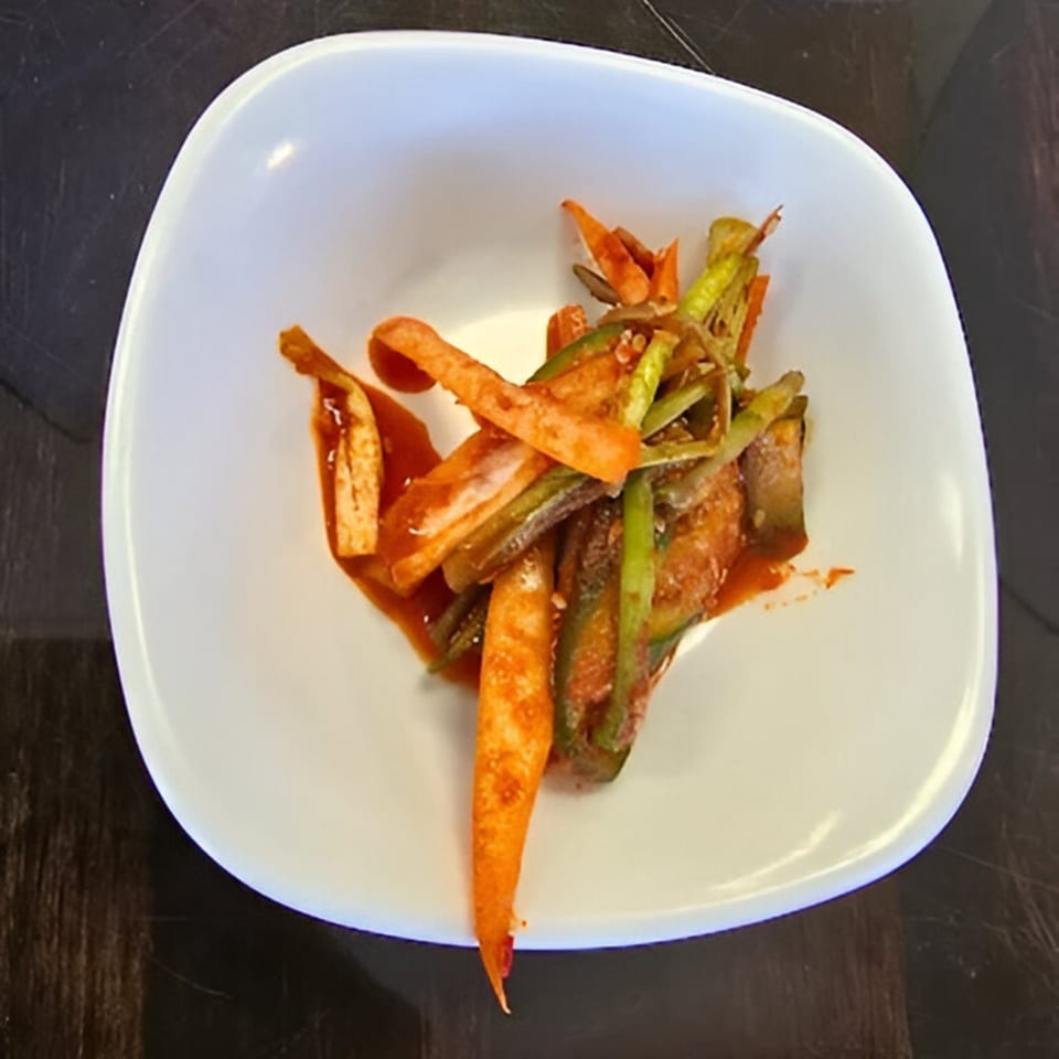 A white bowl filled with Korean pickled vegetables, including orange carrots and green cucumbers.