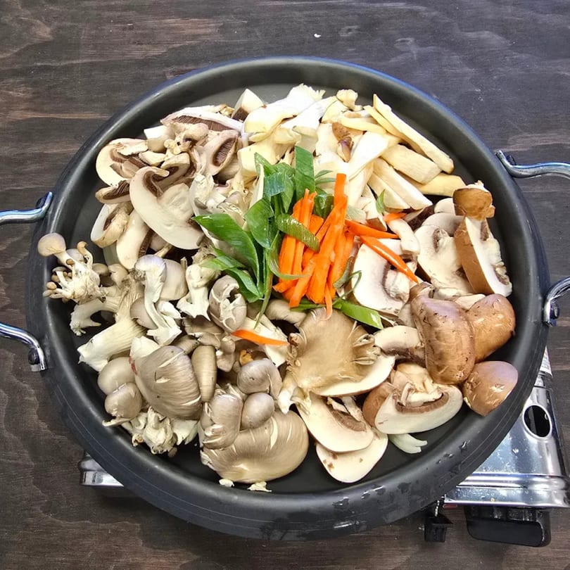 Assorted mushrooms, carrots, and green onions in a black pan, ready for Korean cooking.
